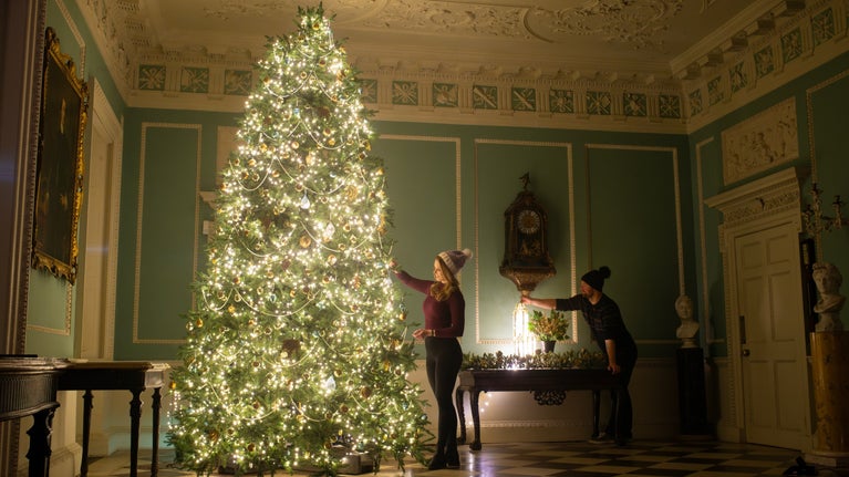 two staff members decorate the Entrance Hall Christmas tree at Saltram